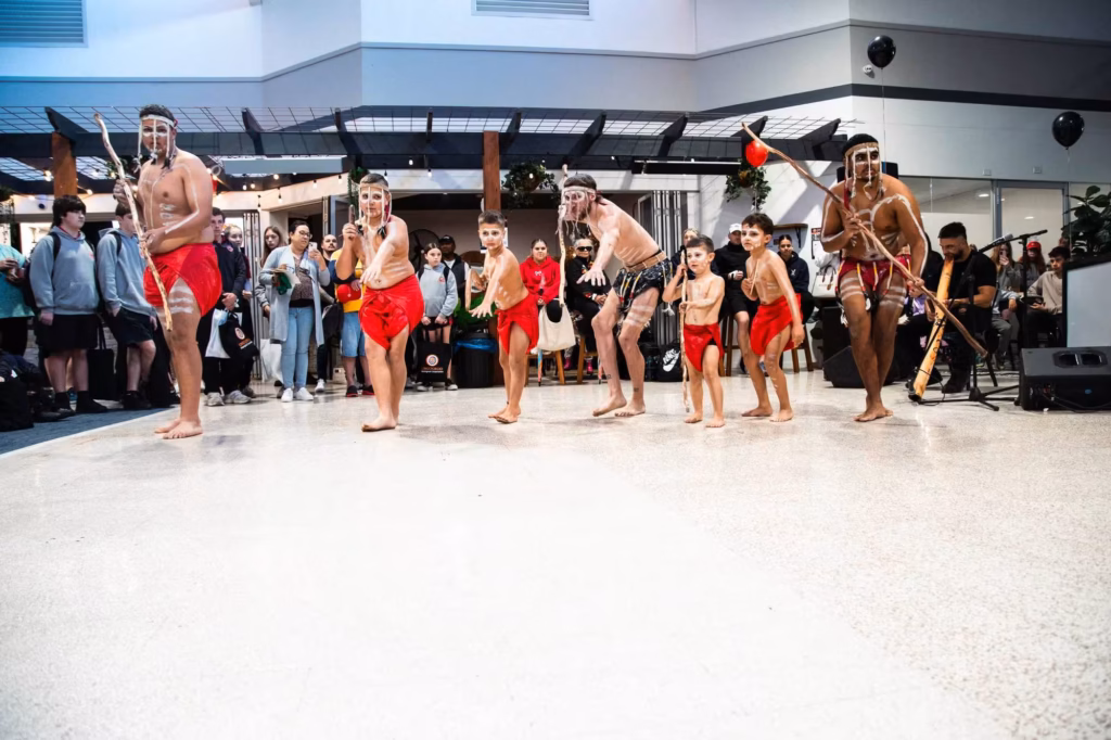 Indigenous Australian dancers performing a traditional dance in front of an audience.